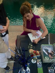 Beautiful woman signing a book at a book signing event, promoting Dr. Tammy Bradshaw-Scott's work in health and wellness.