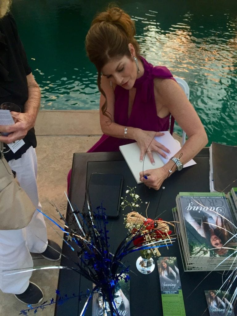 Beautiful woman signing a book at a book signing event, promoting Dr. Tammy Bradshaw-Scott's work in health and wellness.